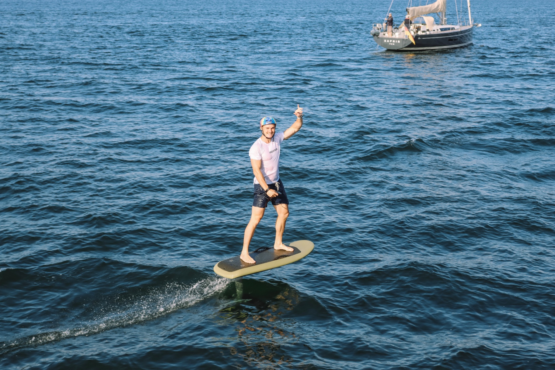 E-foil rider gliding past a sailboat on the Baltic Sea near Fehmarn